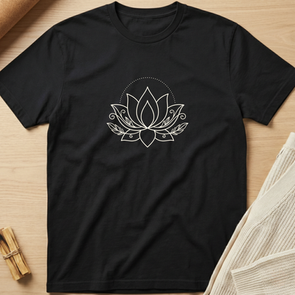 A black short-sleeve crewneck t-shirt with a white line art lotus flower graphic on the chest, laid flat on a light wood background with styled props. Minimalist yoga apparel by pemuyo.