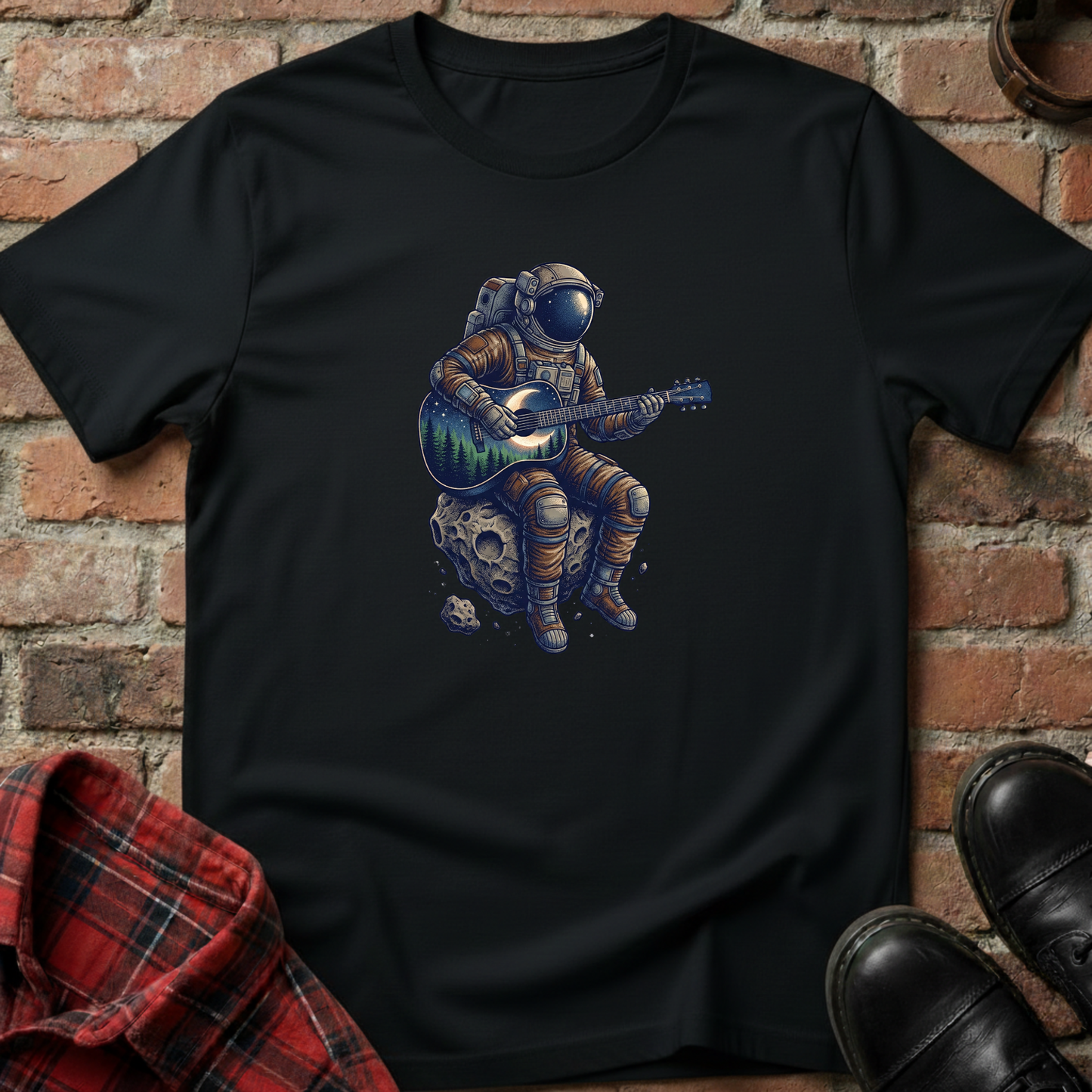 Black t-shirt with an astronaut playing guitar on a moon graphic against a brick wall. Minimalist music apparel by pemuyo.