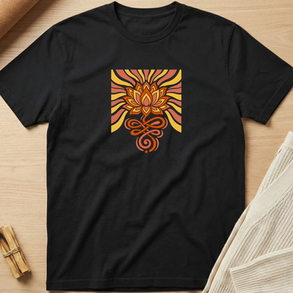 A black short-sleeve crewneck t-shirt laid flat on a light wood surface, featuring a retro-style square graphic on the chest with a lotus flower and swirling sunburst patterns in orange, yellow, and red. Minimalist yoga apparel by pemuyo.
