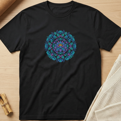 A black short-sleeve crewneck t-shirt laid flat on a light wood surface, featuring a colorful circular mandala graphic in shades of blue, teal, and purple on the chest. Minimalist yoga apparel by pemuyo.