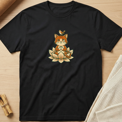 A black short-sleeve crewneck t-shirt laid flat on a light wood surface, featuring a central graphic of a meditating orange cat sitting on a lotus flower with a small bird on its head. Minimalist yoga apparel by pemuyo.