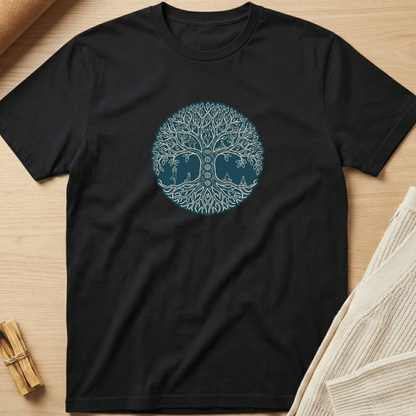 A black short-sleeve crewneck t-shirt laid flat on a light wood surface, featuring a circular tree-of-life graphic in light blue and dark blue on the chest. The shirt is styled with a beige knit fabric and small wooden props in the corners. Minimalist yoga apparel by pemuyo.