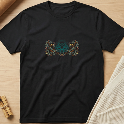 A black short-sleeve crewneck t-shirt laid flat on a light wood surface, featuring a central teal and orange lotus flower graphic with floral details. Minimalist yoga apparel by pemuyo.