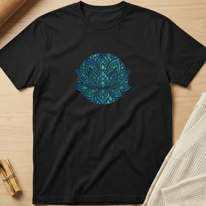 A black short-sleeve crewneck t-shirt laid flat on a light wood surface, featuring a colorful circular mandala graphic in shades of blue, teal, and purple on the chest. Minimalist yoga apparel by pemuyo.