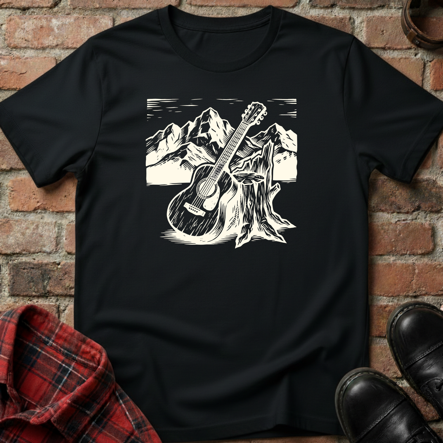 Black t-shirt with a white graphic of a guitar leaning against a tree stump with mountains in the background, displayed on a brick surface. Minimalist music apparel by pemuyo.
