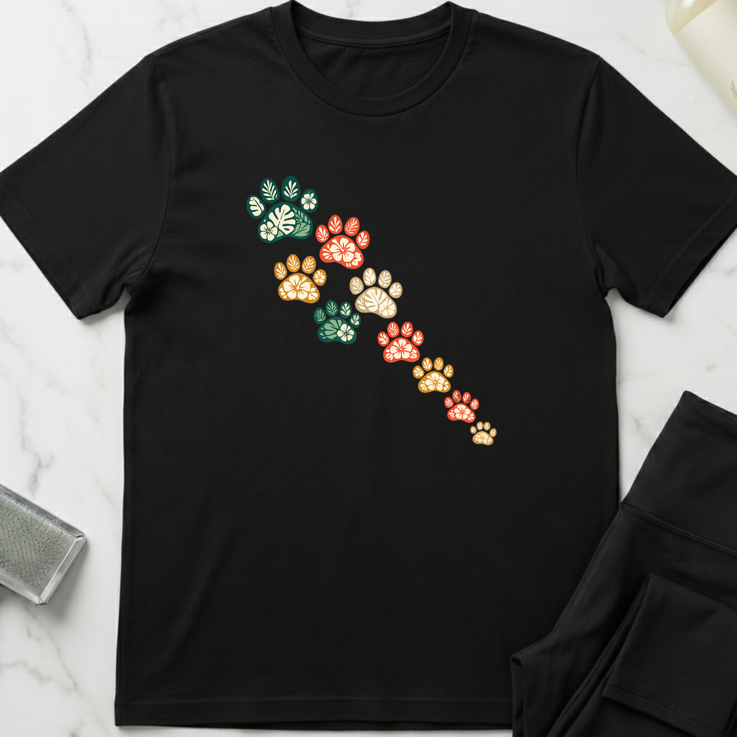 Black t-shirt with colorful paw print design on a marble surface. Minimalist dog apparel by pemuyo.
