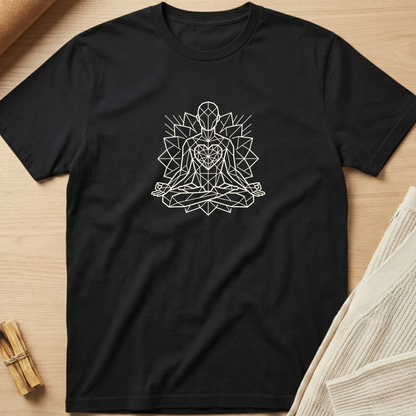 A black short-sleeve t-shirt with a white geometric line art graphic of a meditating figure, laid flat on a light wood background with styled props. Minimalist yoga apparel by pemuyo.