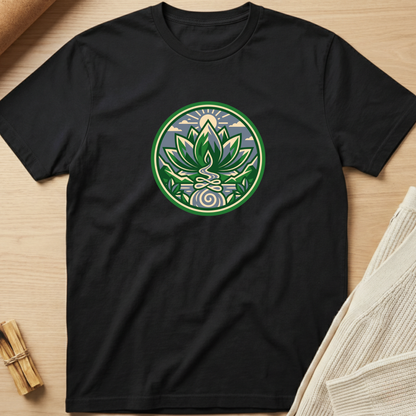 A black short-sleeve crewneck t-shirt laid flat on a light wood surface, featuring a circular green and white lotus medallion graphic printed on the chest. Minimalist yoga apparel by pemuyo.