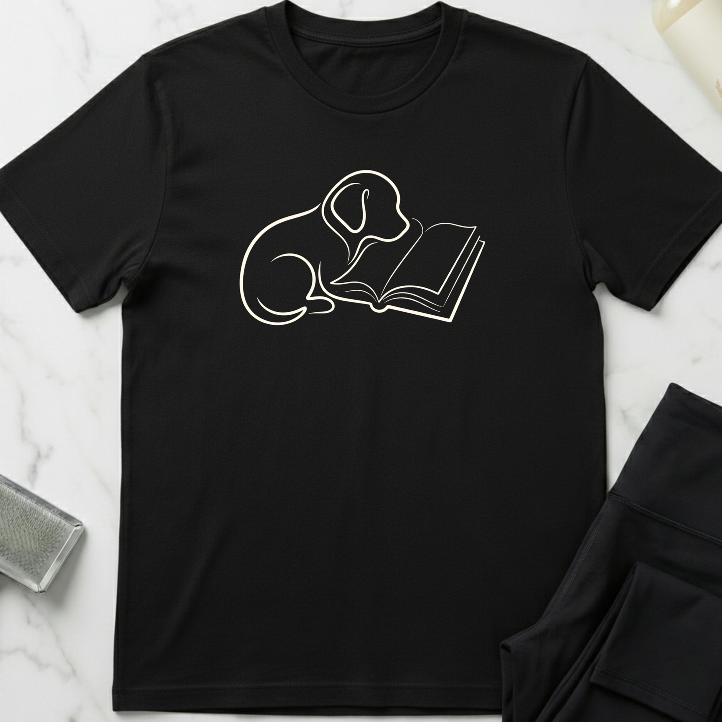 Black t-shirt with a white line drawing of a dog reading a book on a marble surface. Minimalist dog apparel by pemuyo.