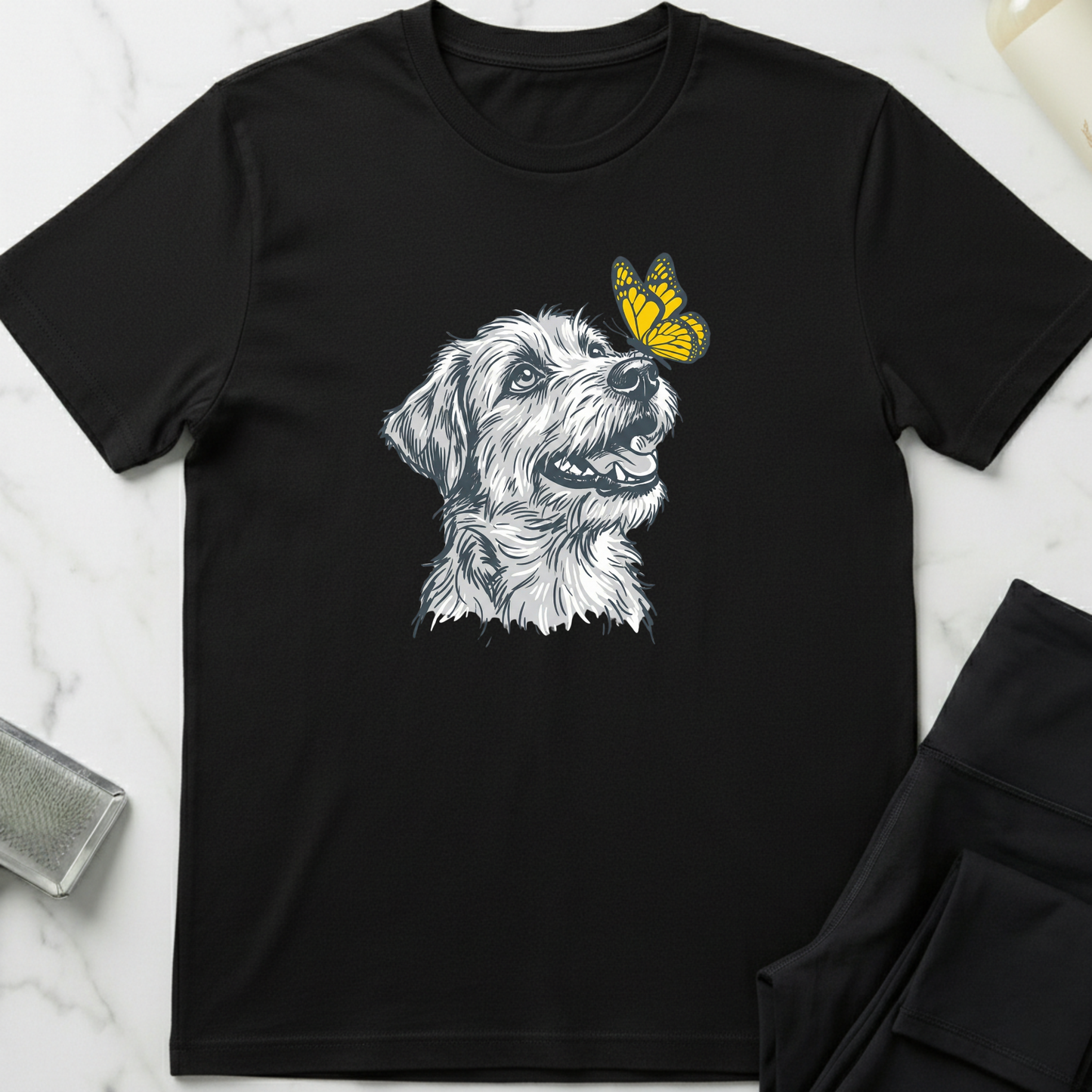 Black t-shirt with a dog and butterfly graphic on a marble surface. Minimalist dog apparel by pemuyo.