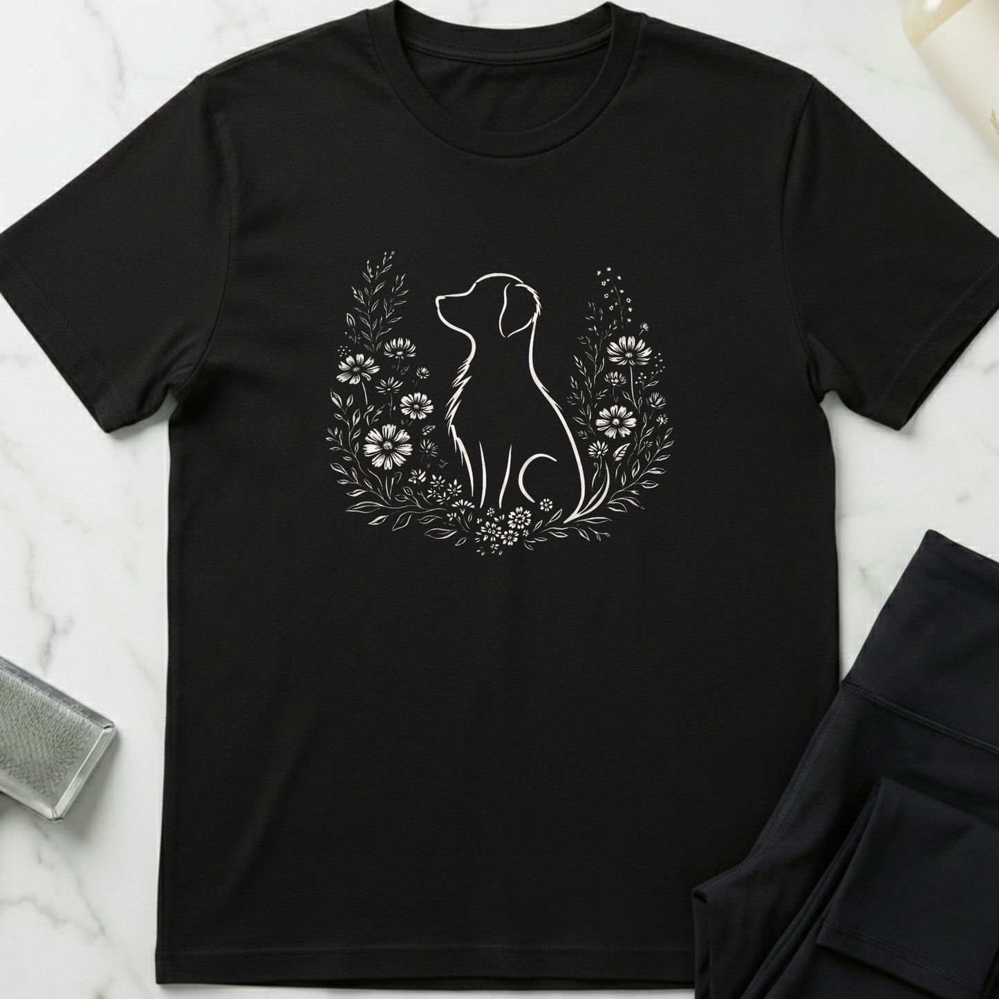 Black t-shirt with a white dog and floral design on a marble surface. Minimalist dog apparel by pemuyo.