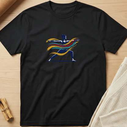 A black short-sleeve crewneck t-shirt laid flat on a light wood background, featuring a colorful graphic of a running superhero silhouette with flowing yellow, orange, and red hair or cape details. Minimalist yoga apparel by pemuyo.