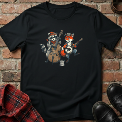 Black t-shirt with cartoon raccoon and fox playing instruments on a brick wall background. Minimalist music apparel by pemuyo.