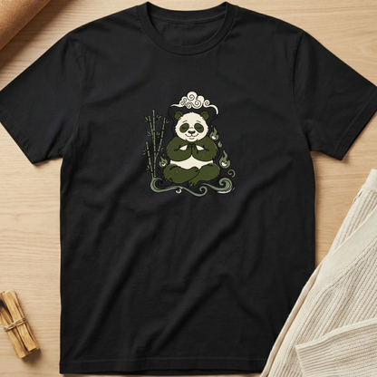 A black short-sleeve crewneck t-shirt laid flat on a light wood surface, featuring a central graphic of a panda meditating with bamboo and a decorative headpiece. Minimalist yoga apparel by pemuyo.