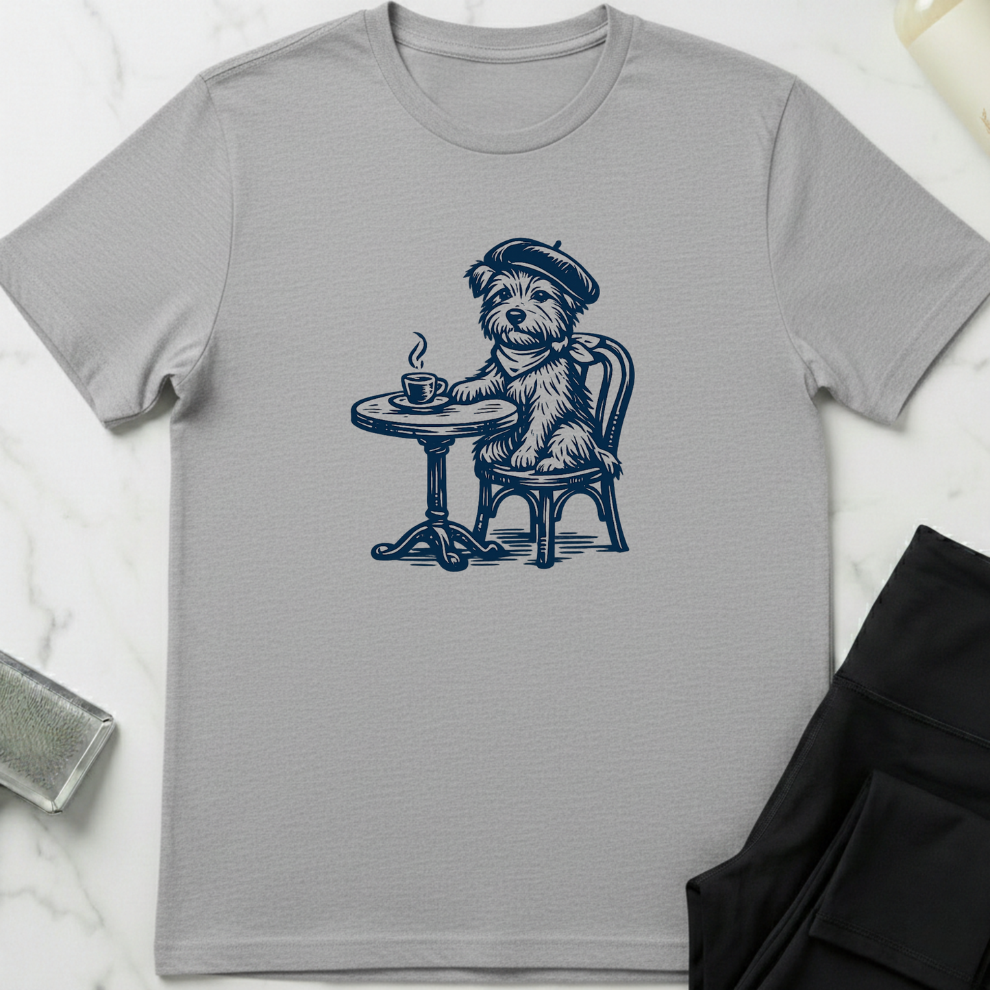 Gray t-shirt with a dog illustration sitting at a table with a cup of coffee on a white marble surface. Minimalist dog apparel by pemuyo.