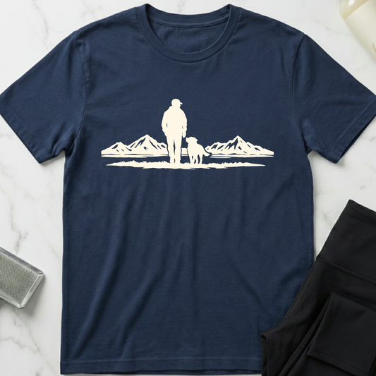 Navy blue t-shirt with white graphic of a person and dog by mountains on a marble surface. Minimalist dog apparel by pemuyo.