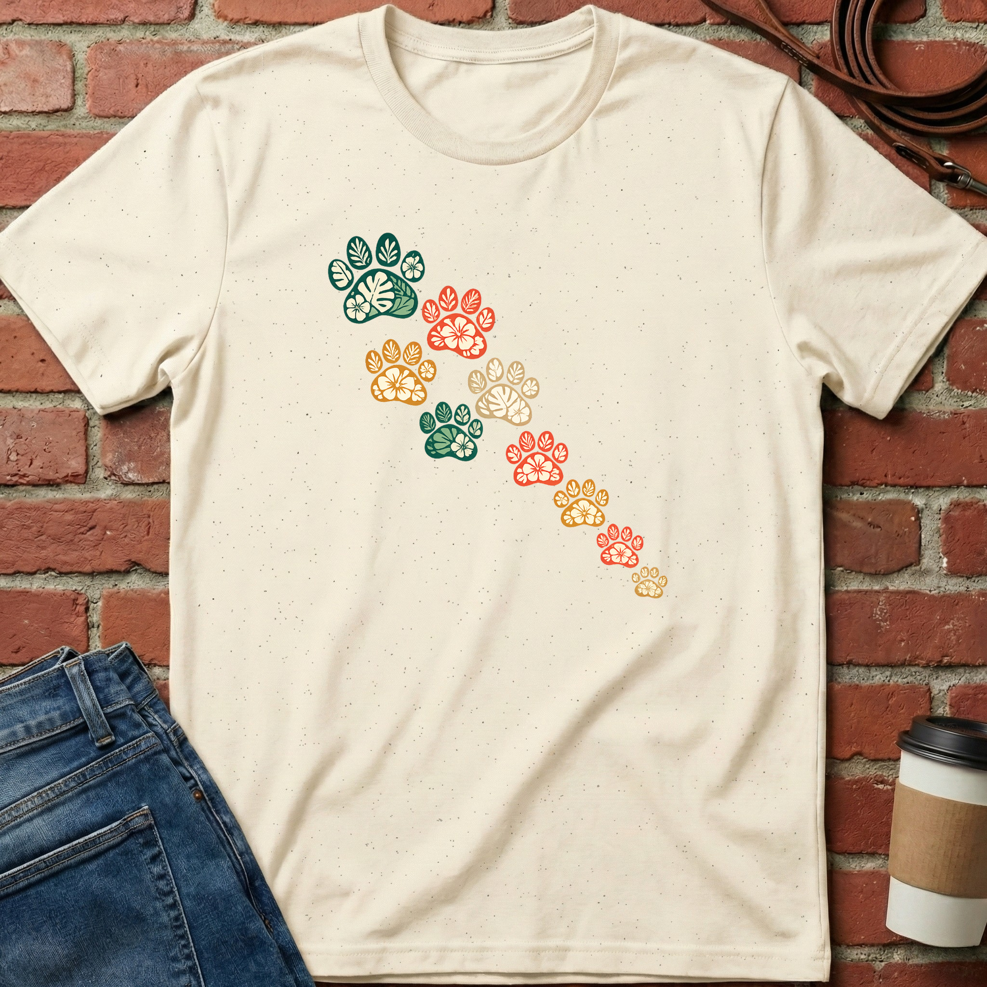 Beige t-shirt with colorful paw print design on a brick wall background. Minimalist dog apparel by pemuyo.