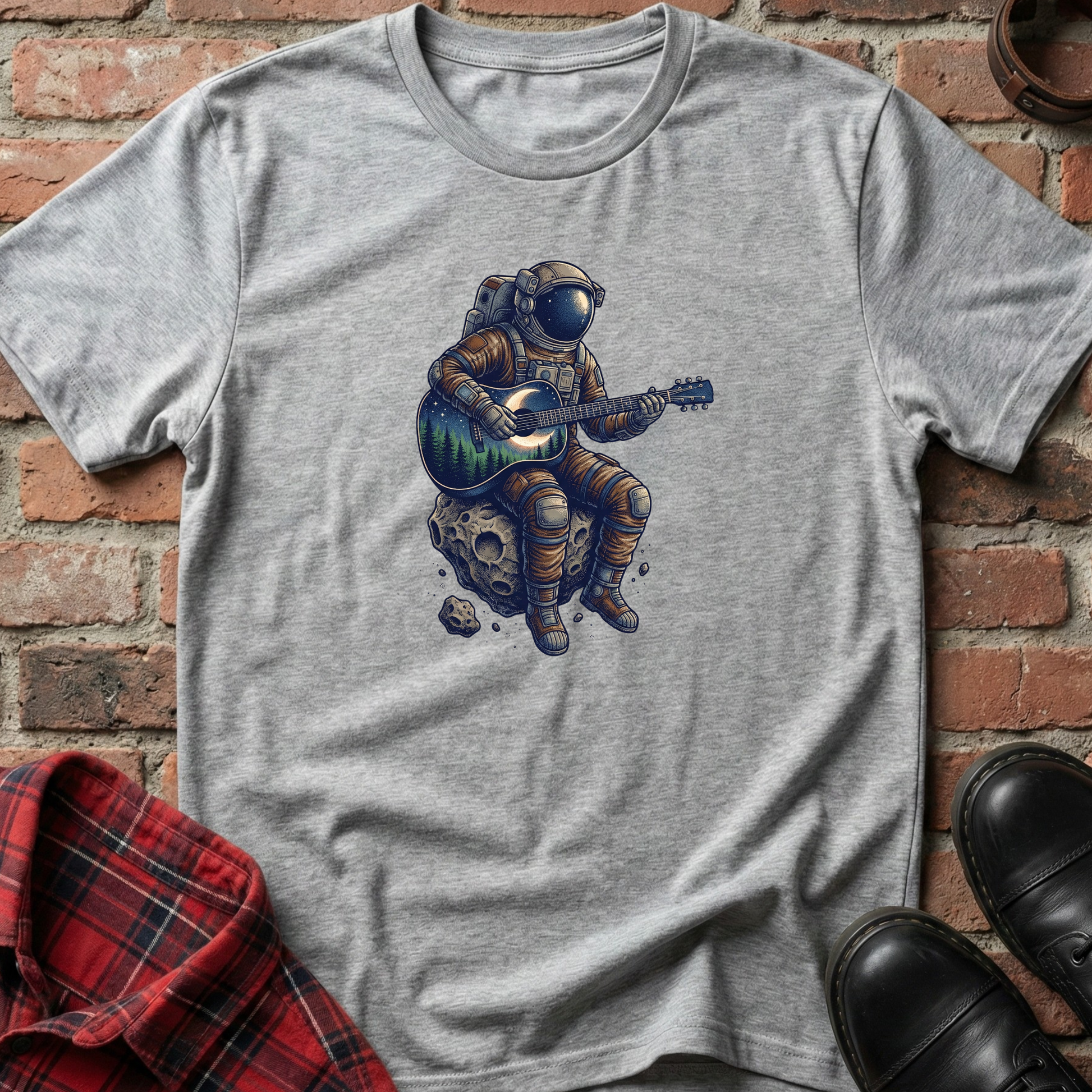 Gray t-shirt with an astronaut playing guitar on a rock design, placed against a brick wall. Minimalist music apparel by pemuyo.