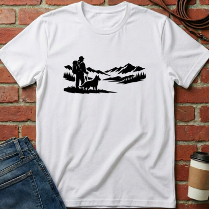 White t-shirt with black graphic design of a couple and dog against a mountainous landscape, placed on a brick surface. Minimalist dog apparel by pemuyo.