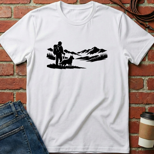 White t-shirt with black graphic design of a couple and dog against a mountainous landscape, placed on a brick surface. Minimalist dog apparel by pemuyo.