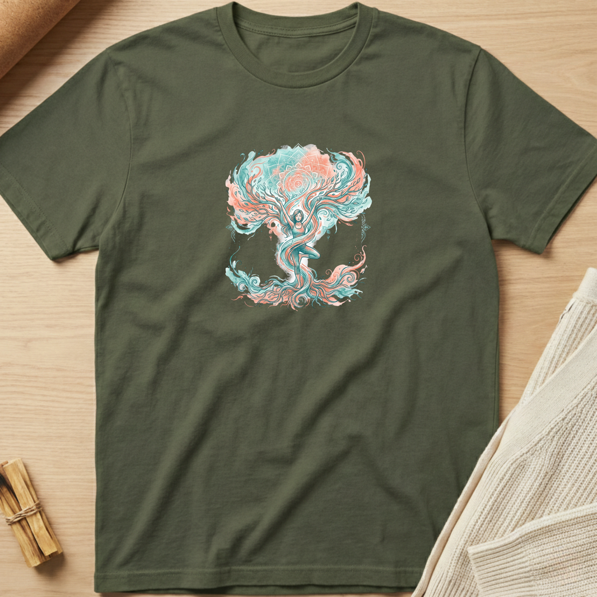 An olive green crewneck t-shirt featuring a colorful psychedelic tree of life graphic in teal and pink, laid flat on a light wood background with styled props. Minimalist yoga apparel by pemuyo.