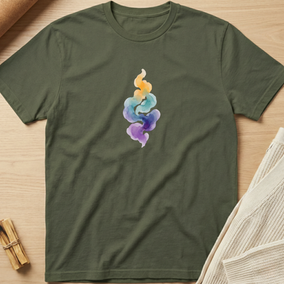 An olive green short-sleeve t-shirt with a colorful watercolor-style abstract graphic on the chest, laid flat on a light wood background with styled props. Minimalist yoga apparel by pemuyo.