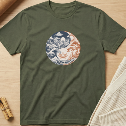An olive green short-sleeve t-shirt laid flat on a light wood surface, featuring a circular yin-yang style graphic on the chest with blue ocean waves and a pink lotus flower on one side and a pink tree on the other. Minimalist yoga apparel by pemuyo.