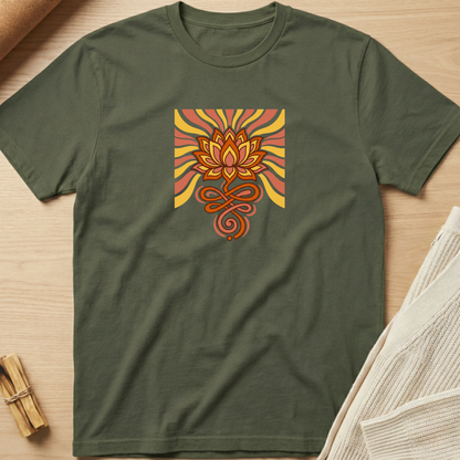 An olive green short-sleeve t-shirt laid flat on a light wood surface, featuring a square graphic print of a stylized lotus flower in orange, yellow, and red with radiating stripes. Minimalist yoga apparel by pemuyo.