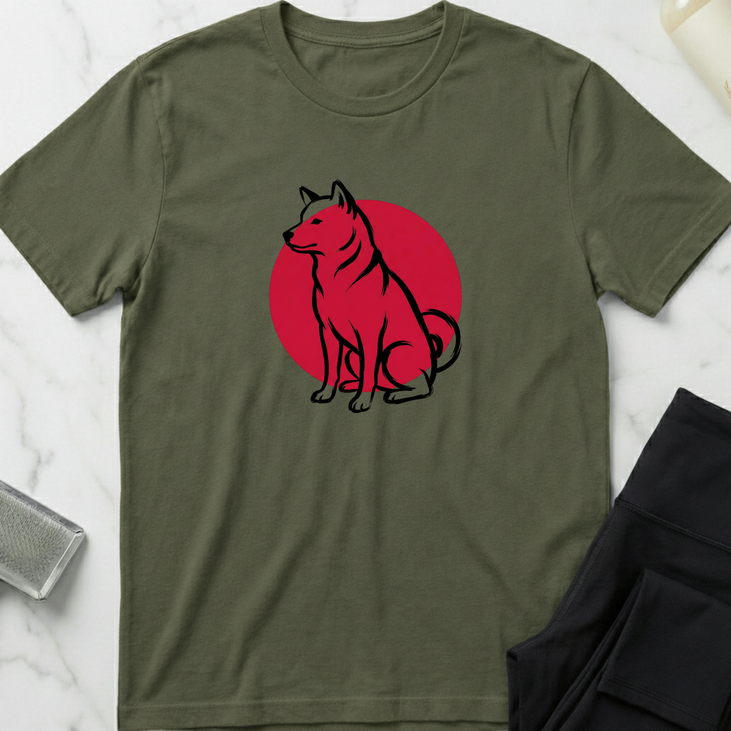 Green t-shirt with a dog graphic on a red circle, placed on a marble surface. Minimalist dog apparel by pemuyo.