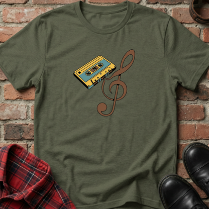 Green t-shirt with a cassette tape and treble clef design against a brick wall. Minimalist music apparel by pemuyo.