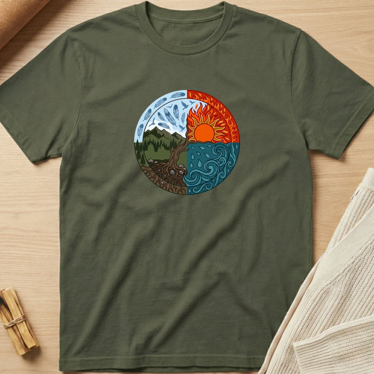 An olive green short-sleeve t-shirt laid flat on a light wood surface, featuring a circular yin-yang style graphic on the chest with a tree, mountains, sun, and blue water elements. Minimalist yoga apparel by pemuyo.
