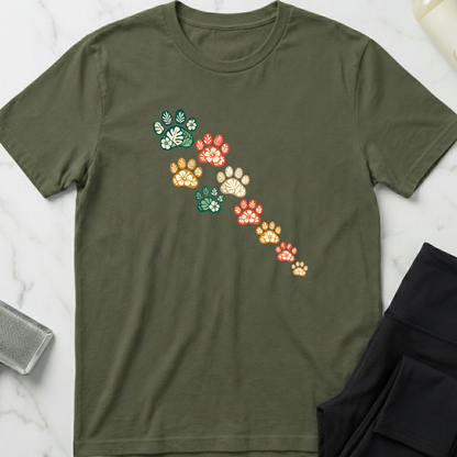 Green t-shirt with colorful paw print design on a marble surface. Minimalist dog apparel by pemuyo.