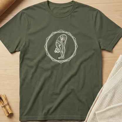 An olive green short-sleeve t-shirt with a white line art graphic of a person in a yoga forward bend pose inside a geometric circle, laid flat on a light wood background with styled props. Minimalist yoga apparel by pemuyo.