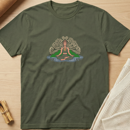 An olive green short-sleeve t-shirt with a colorful graphic of a meditating figure, laid flat on a light wood background with styled props. Minimalist yoga apparel by pemuyo.