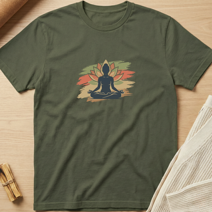 An olive green short-sleeve t-shirt laid flat on a light wood surface, featuring a central graphic of a meditating silhouette in front of a stylized lotus flower in muted green, orange, and beige tones. Minimalist yoga apparel by pemuyo.