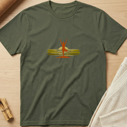 An olive green crewneck t-shirt laid flat on a light wood surface, featuring a central graphic of a red silhouette of a person standing on yellow and gold horizontal brushstrokes. Minimalist yoga apparel by pemuyo.