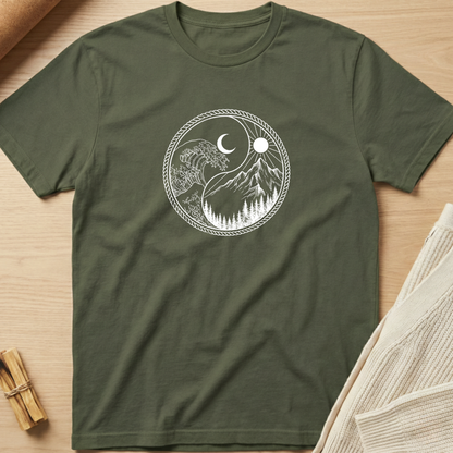 An olive green short-sleeve t-shirt with a white circular graphic of a yin-yang symbol featuring a tree, mountains, moon, and sun, laid flat on a light wood background with styled props. Minimalist yoga apparel by pemuyo.
