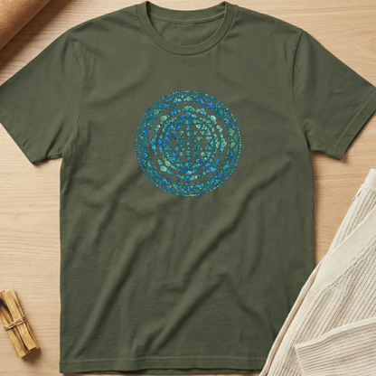 An olive green crewneck t-shirt with a circular mandala pattern in shades of blue and teal on the chest, laid flat on a light wood background with styled props. Minimalist yoga apparel by pemuyo.