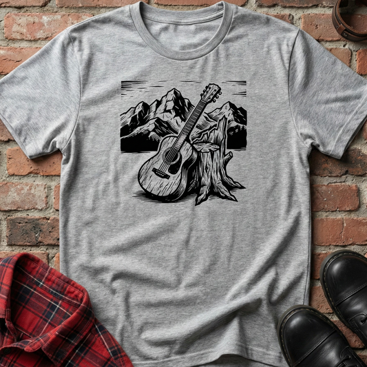Gray t-shirt with a guitar graphic on a brick wall background. Minimalist music apparel by pemuyo.