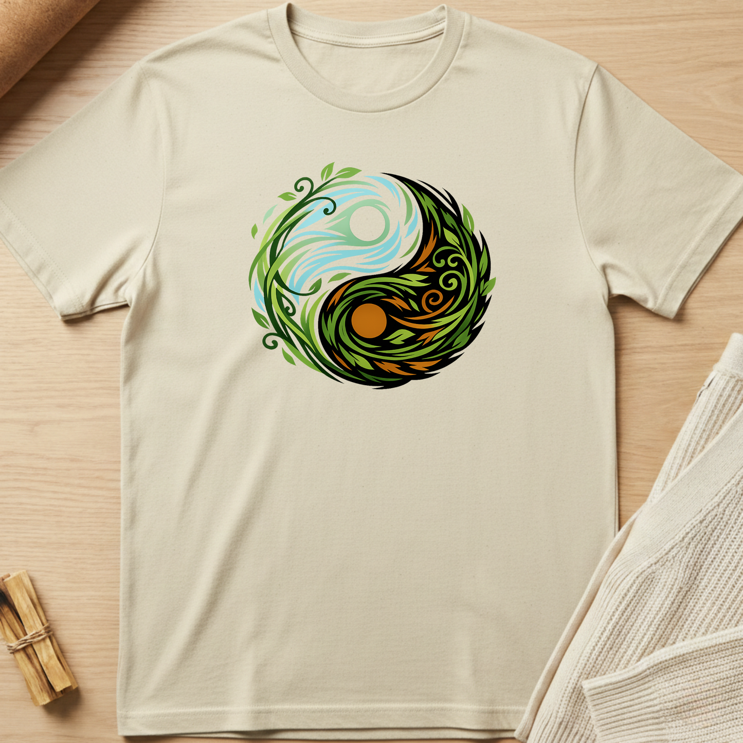 Beige t-shirt with a yin yang design featuring nature elements on a wooden surface. Minimalist yoga apparel by pemuyo.