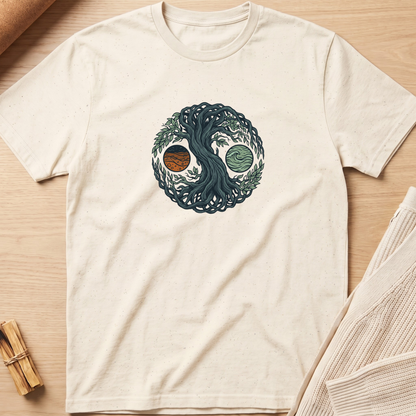 An off-white short-sleeve t-shirt laid flat on a light wood surface, featuring a circular yin-yang style graphic with a dark blue tree and two planets. Minimalist yoga apparel by pemuyo.