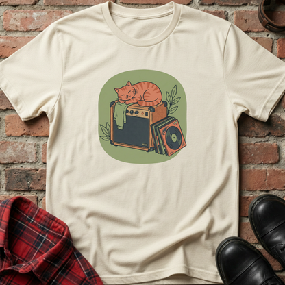 Beige t-shirt with a graphic of a cat on an amplifier against a brick wall. Minimalist music apparel by pemuyo.