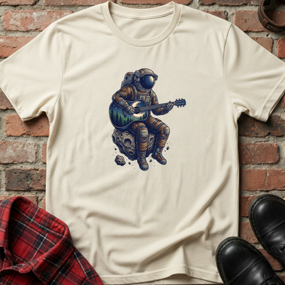 Beige t-shirt with an astronaut playing guitar on a rock graphic against a brick wall. Minimalist music apparel by pemuyo.