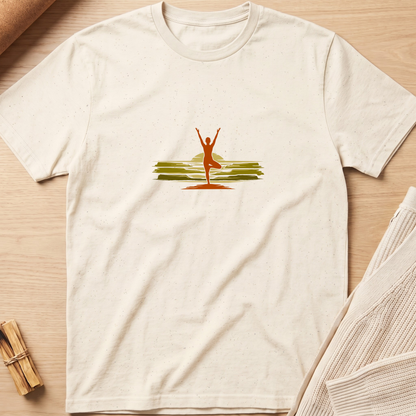 An off-white short-sleeve t-shirt with a small graphic of a yoga pose against a sunset on the chest, laid flat on a light wood background with styled props. Minimalist yoga apparel by pemuyo.