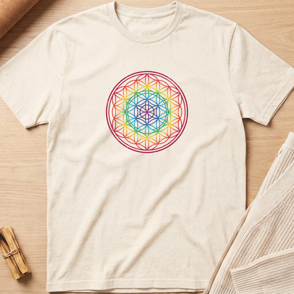 An off-white short-sleeve t-shirt with a colorful geometric flower design printed on the chest, laid flat on a light wood background with neutral props. Minimalist yoga apparel by pemuyo.