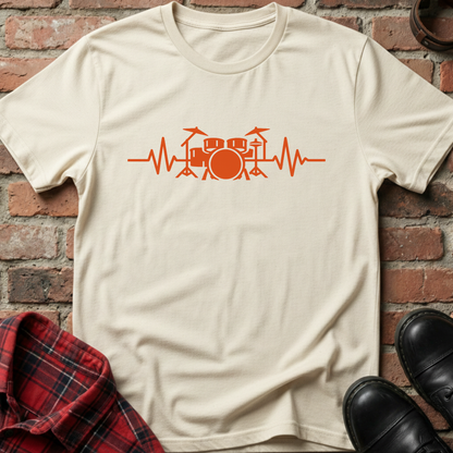 Beige t-shirt with orange drum set heartbeat design on a brick wall background. Minimalist music apparel by pemuyo.