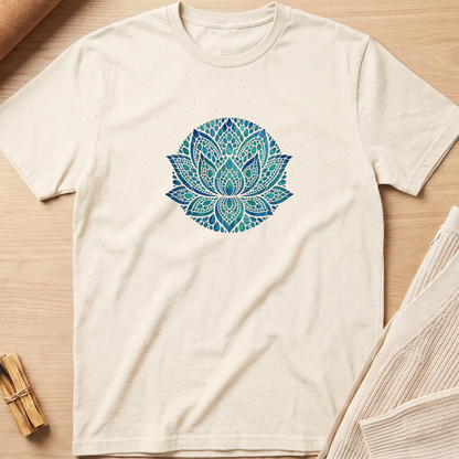 An off-white short-sleeve t-shirt with a blue and teal mandala lotus print on the chest, laid flat on a light wood background with neutral props. Minimalist yoga apparel by pemuyo.