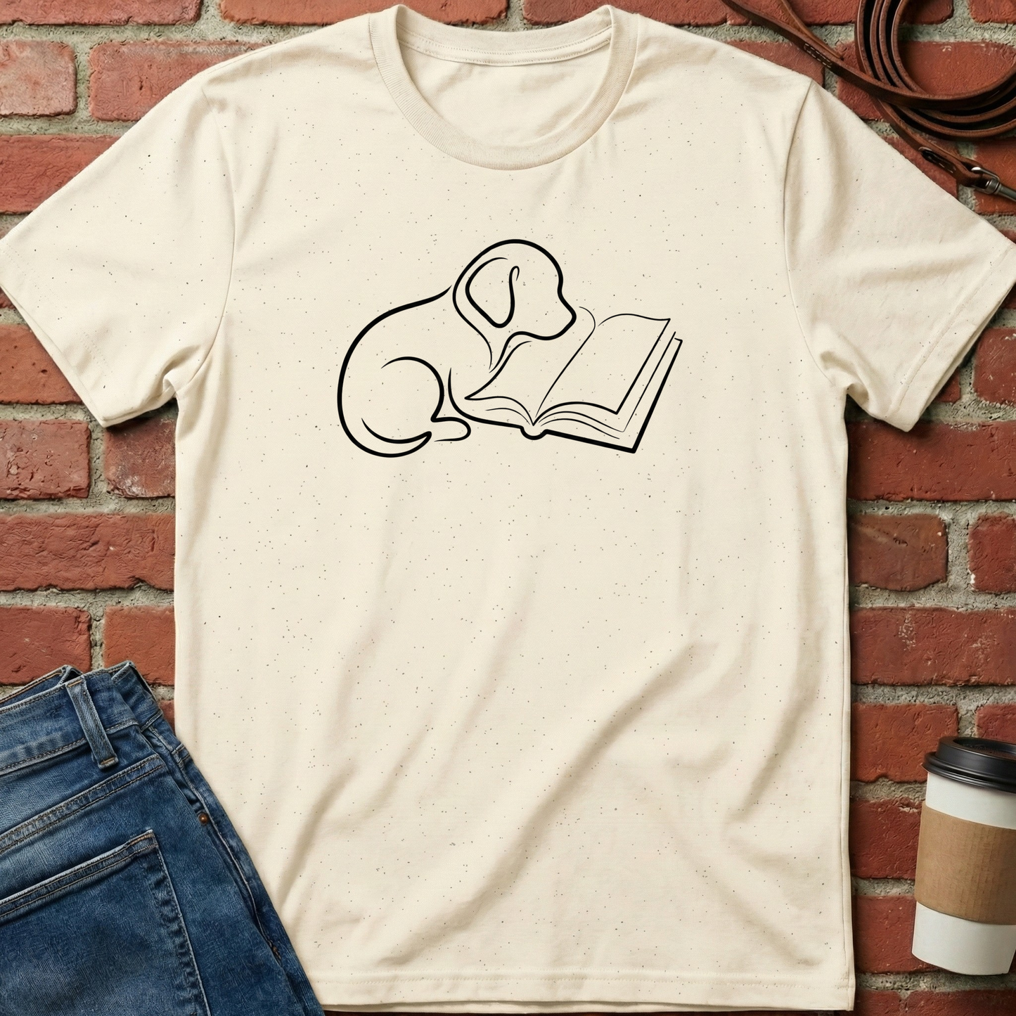 Beige t-shirt with a dog reading a book graphic on a brick wall background. Minimalist dog apparel by pemuyo.