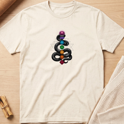 An off-white short-sleeve t-shirt laid flat on a light wood background, featuring a graphic of a black coiled snake wrapped around the chakras with colorful gemstone details. Minimalist yoga apparel by pemuyo.