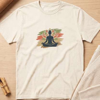 An off-white short-sleeve t-shirt with a colorful graphic of a meditating silhouette in front of a lotus flower, laid flat on a light wood background. Minimalist yoga apparel by pemuyo.